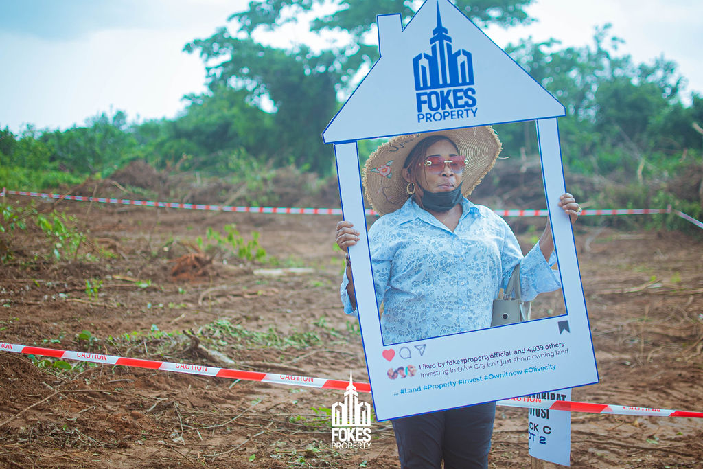 Female agent holding 'Now a House Owner' sign after land purchase at Olive City